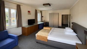 A hotel room with a bed, a desk, a television, a sofa, and a view of the outside.