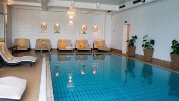 An indoor swimming pool with lounge chairs and potted plants.