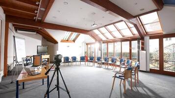 A conference room with a high ceiling, wooden beams, a large skylight, and a view of the outside.