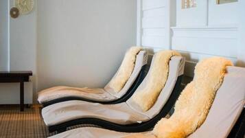 Ein Raum mit drei Liegemassagesesseln, einer Holzbank und einer Wand mit Dekoration.
