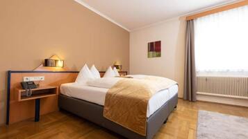 A hotel room with a bed, bedside tables, a telephone, a radiator, and a window with curtains.