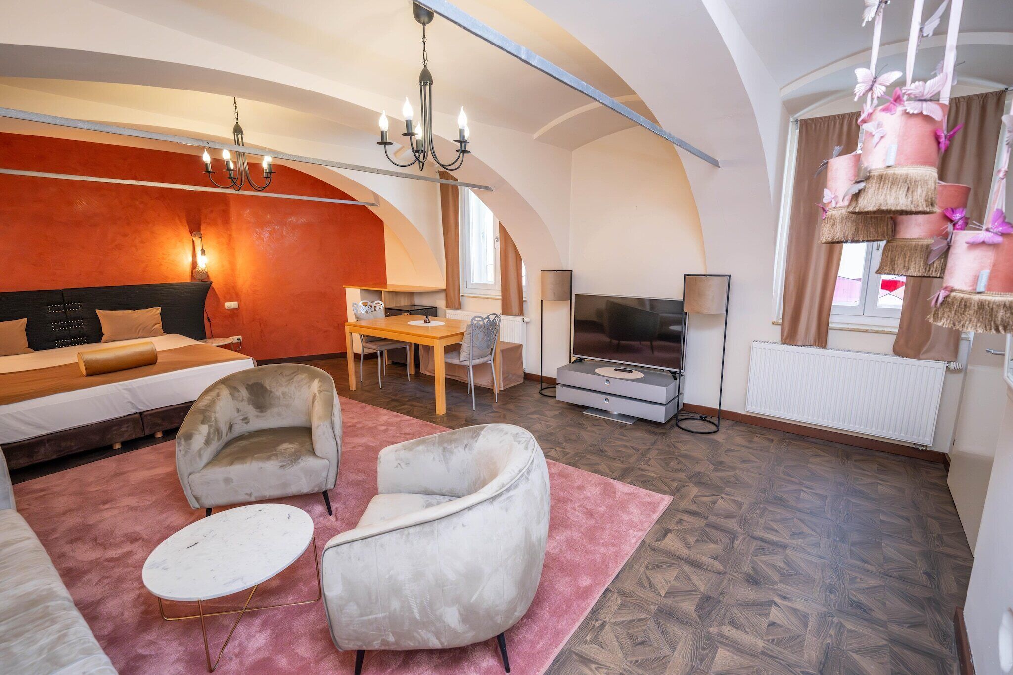 Una sala de estar moderna con un sofá, dos sillones, una mesa de comedor, un televisor y una araña.