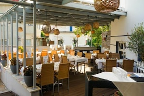 An outdoor dining area with tables and chairs, covered by a pergola, and potted plants along the walls. - Hotel Landliebe by Belvilla Junior Suite (Söchau)