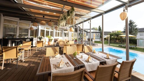 Eine Terrassengaststätte mit Tischen, Stühlen, einem Pool und einem überdachten Bereich mit hängenden Pflanzen.