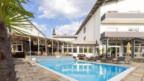 Ein Poolbereich mit überdachter Sitzgelegenheit, einem Pool und einem Gebäude mit Balkonen.