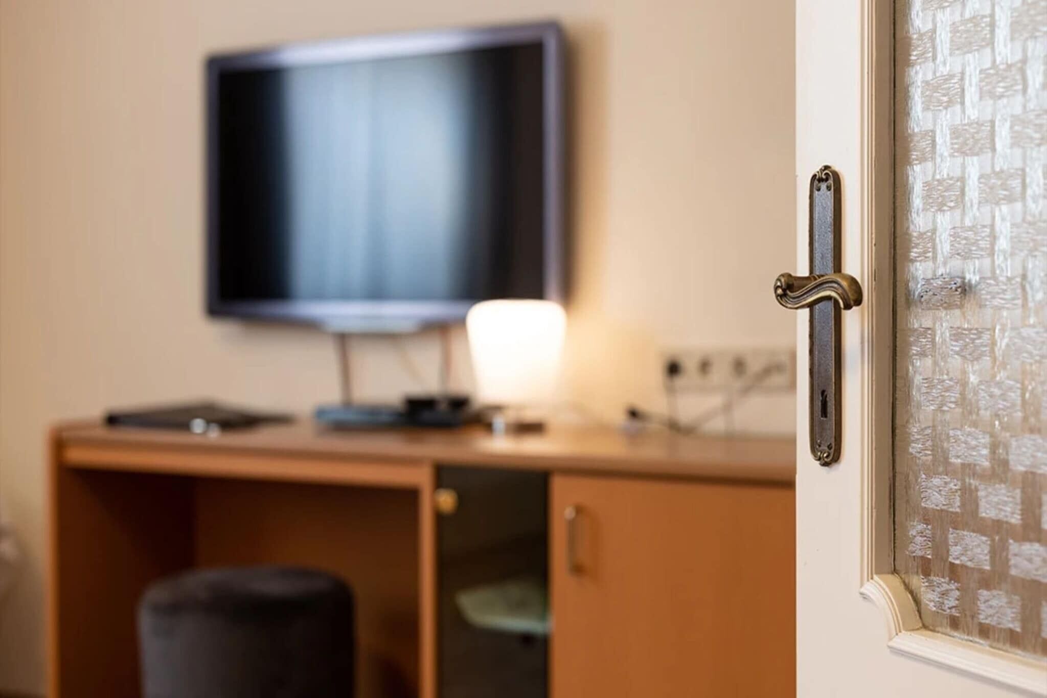 A room with a television mounted on the wall, a desk with a lamp, and a door with a textured glass panel.