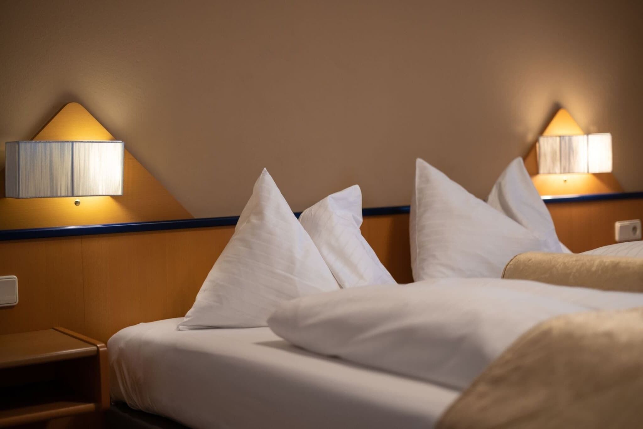 Ein Hotelzimmer mit einem Bett, Kissen, einem Nachttisch und Wandlampen.