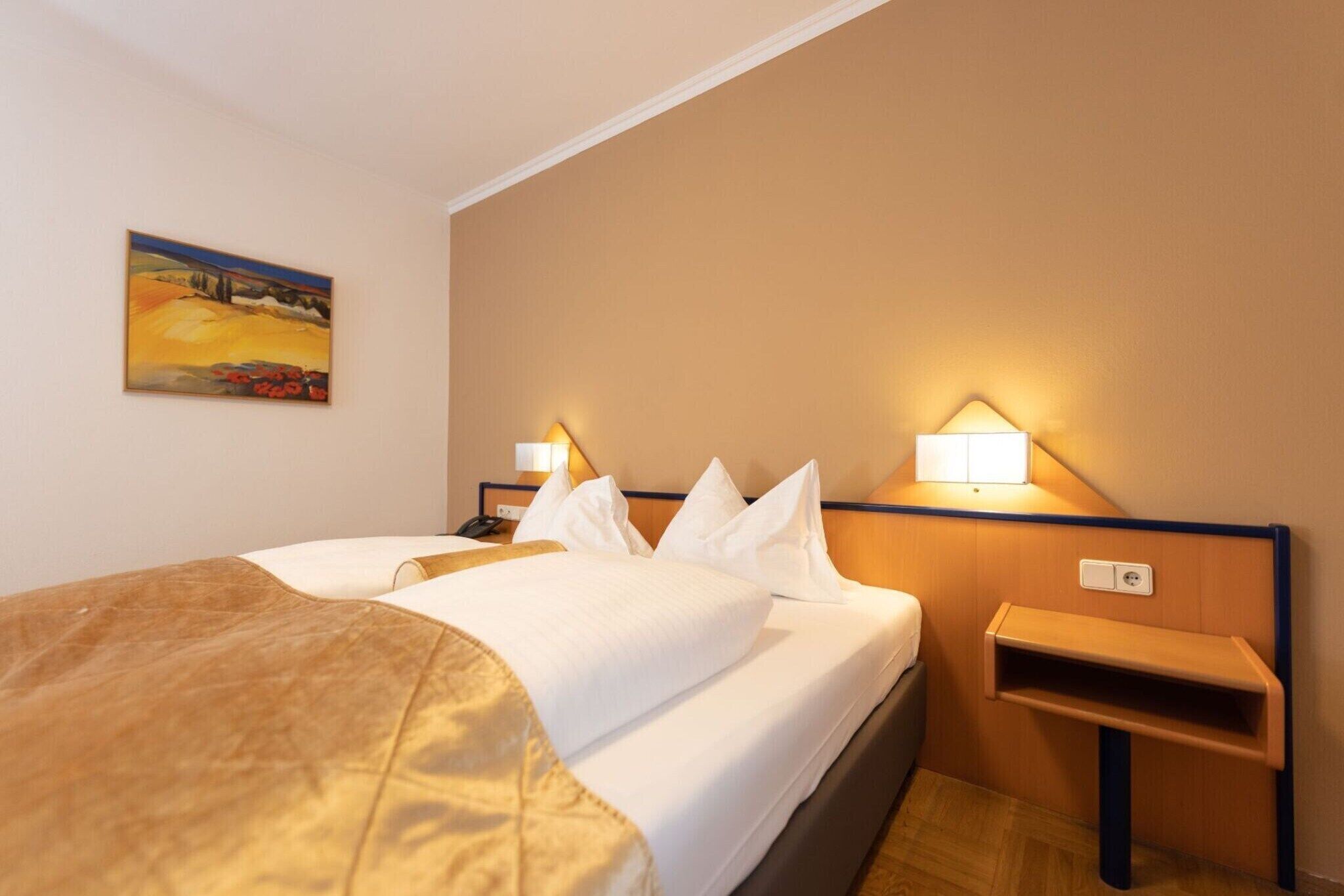 Een hotelkamer met een bed, nachtlampjes, een schilderij aan de muur en een klein houten nachtkastje.