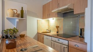 Une cuisine avec des meubles en bois, un réfrigérateur en acier inoxydable, un lave-vaisselle et un plan de travail agrémenté d’une plante et d’ustensiles.