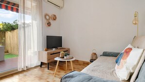 Un salon moderne avec un canapé, un téléviseur, une petite table en bois et une fenêtre avec des rideaux.