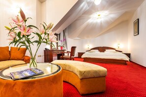 Habitación de hotel con cama, escritorio, silla, mesa de centro de vidrio y un jarrón con flores.