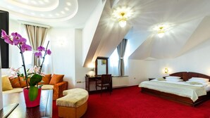 A hotel room with a red carpet, a bed, a desk, a chair, and a sofa. - Garni Hotel Royal Crown (Subotica)