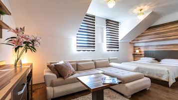 Ein modernes Schlafzimmer mit einem großen Bett, einer Couch und einem kleinen Tisch. Es gibt zwei Fenster mit Jalousien, eine Heizung und eine Deckenleuchte.