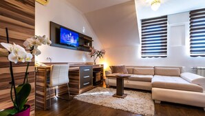 A modern living room with a flat-screen TV, a sofa, a desk with a chair, and a potted plant. - Garni Hotel Royal Crown (Subotica)