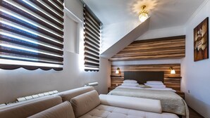 A modern bedroom with a sofa, two beds, wooden paneling, and a chandelier. - Garni Hotel Royal Crown (Subotica)