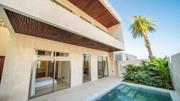 A modern two-story building with a swimming pool, large sliding glass doors, and a palm tree. - Surfside Appartments & Villas (Pecatu)