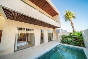A modern two-story building with a swimming pool, large sliding glass doors, and a palm tree. - Surfside Appartments & Villas (Pecatu)