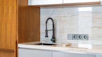 A kitchen with a modern faucet, a sink, and a marble backsplash.