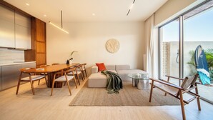 A modern living room with a dining area, a sofa, a coffee table, and a large window. - Surfside Appartments & Villas (Pecatu)