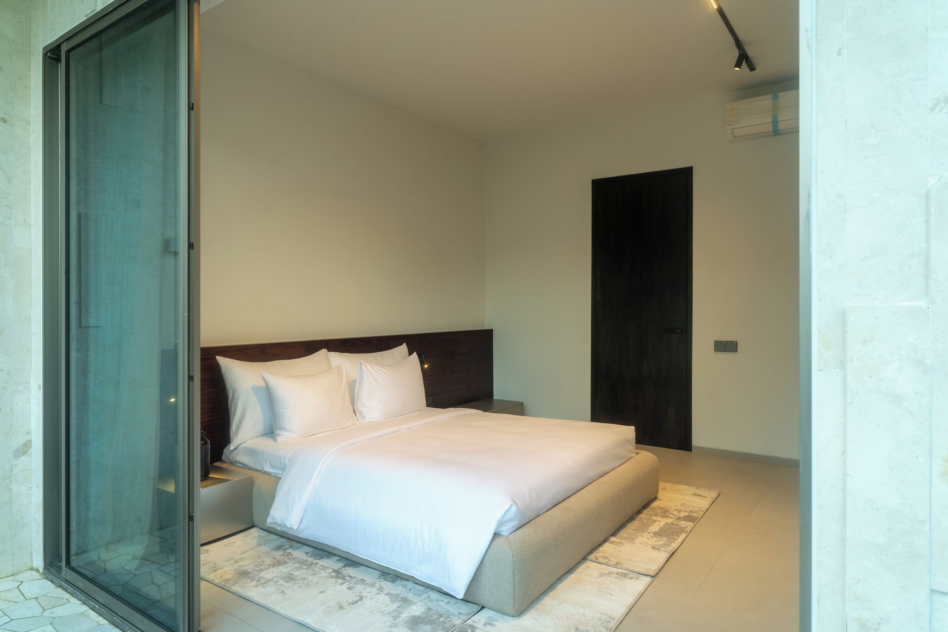 Un dormitorio moderno con una cama, una mesita de noche y un ventanal corredero que da a un balcón.