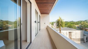 A modern balcony with glass doors, a wooden ceiling, and a view of a green landscape. - Surfside Appartments & Villas (Pecatu)