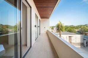 A modern balcony with glass doors, a wooden ceiling, and a view of a green landscape.