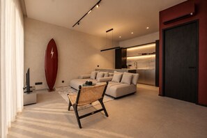 A modern living room with a sofa, a wicker chair, a television, and a surfboard decoration. - Surfside Appartments & Villas (Pecatu)