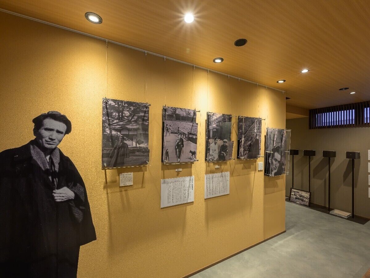 A hallway with a large black and white photograph of a person, several smaller black and white photographs on the wall, and informational plaques.