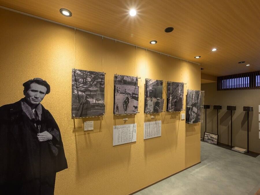 A hallway with a large black and white photograph of a person, several smaller black and white photographs on the wall, and informational plaques.