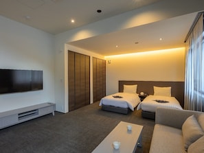 Una habitación de hotel con dos camas, un televisor, una mesa de centro y un ventanal grande.