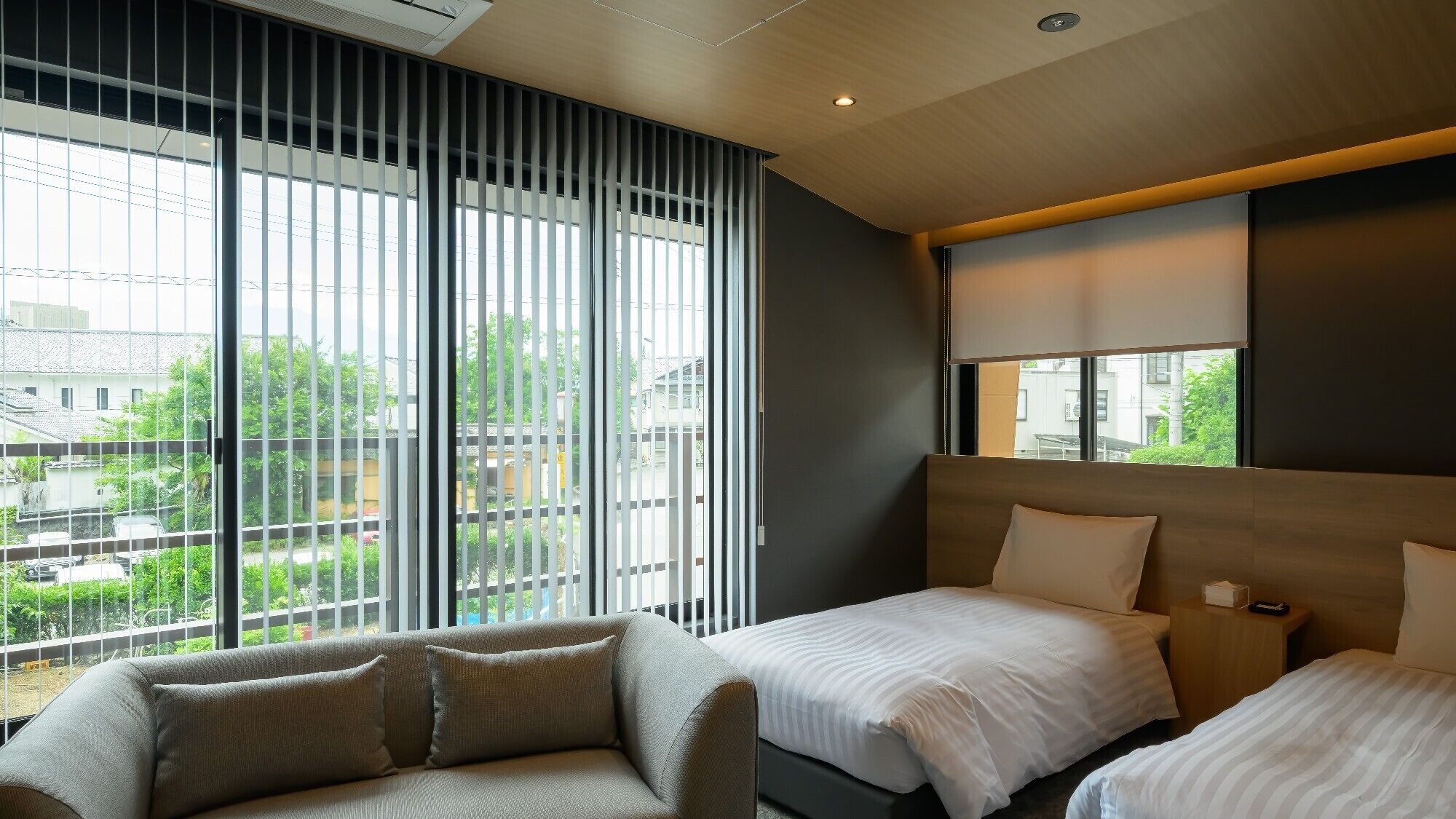 A hotel room with a large window, a sofa, two beds, and a wooden headboard.