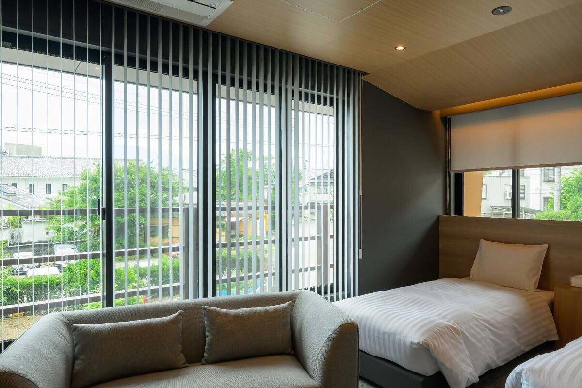 Ein Hotelzimmer mit großem Fenster, einer Couch, zwei Betten und einem Holzkopfende.