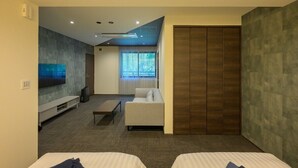 Moderni hotellihuone, jossa on sohva, televisio, vaatekaappi ja sänky.