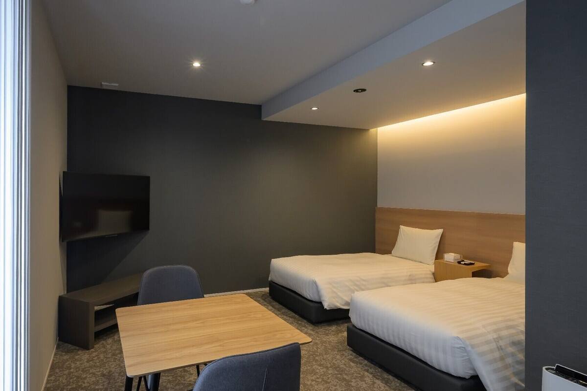 Ein Hotelzimmer mit zwei Betten, einem Fernseher, einem Schreibtisch und einem Sessel.