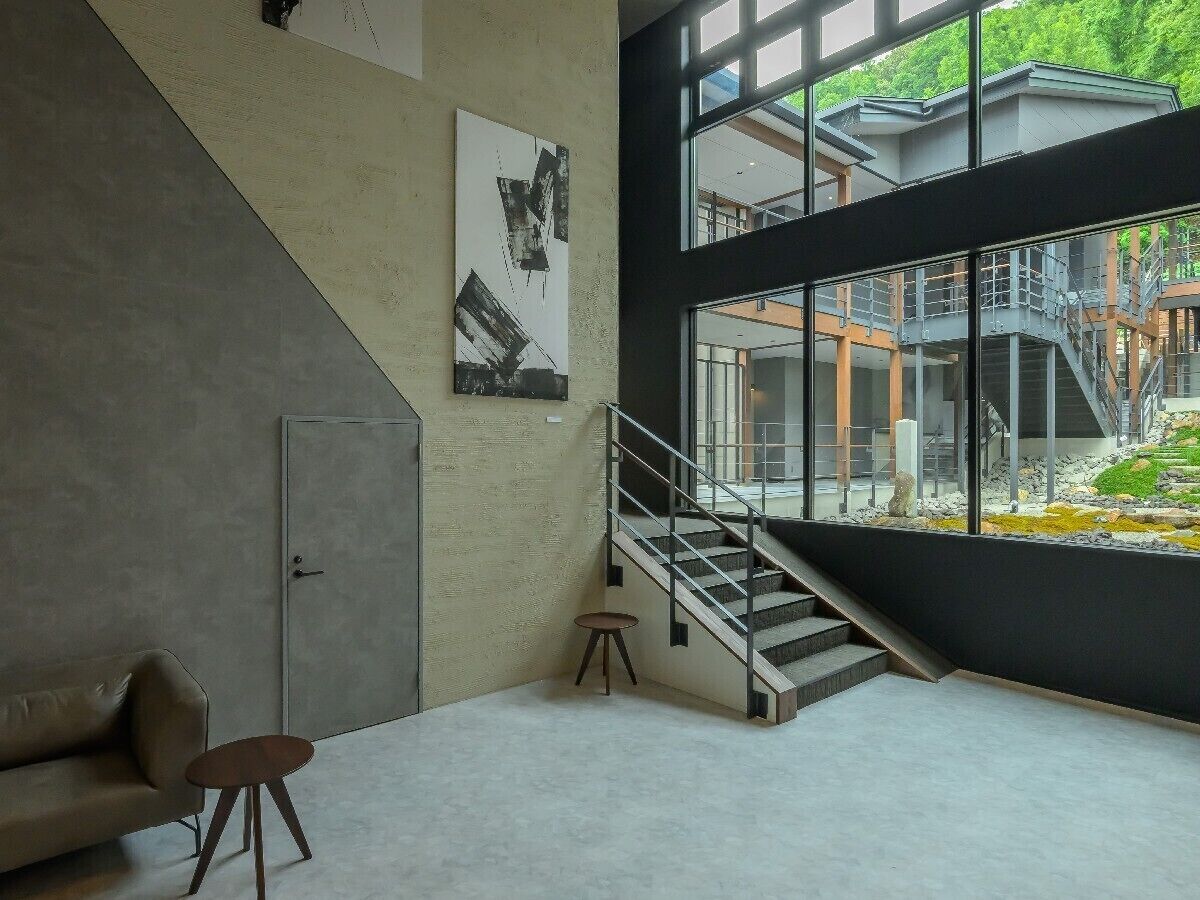 A modern interior with a staircase, a sofa, a small stool, and a painting on the wall.