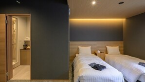 Hotellihuone, jossa on kaksi sänkyä, puuovi, pieni yöpöytä lampun kanssa ja näkyvissä oleva kylpyhuone.