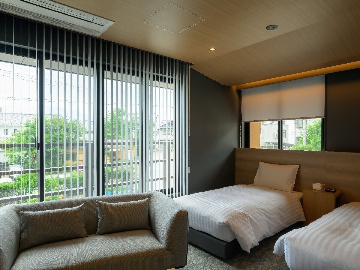 A hotel room with a large window, a sofa, two beds, and a nightstand.