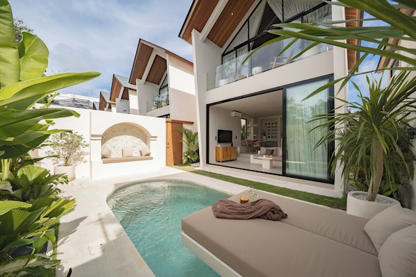 Una casa moderna con piscina, mobiliario exterior y ventanas amplias.
