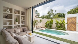 A modern living room with a large sofa, a coffee table, and a pool area visible through a glass door. - Villa Enola Uluwatu (Uluwatu)