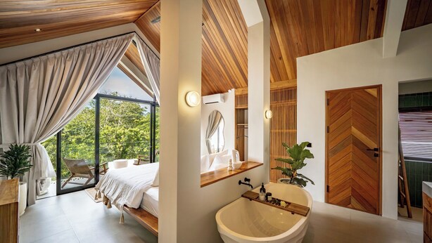 A modern bedroom with a large window, a wooden ceiling, a bed, and a view of greenery. - Villa Enola Uluwatu (Uluwatu)