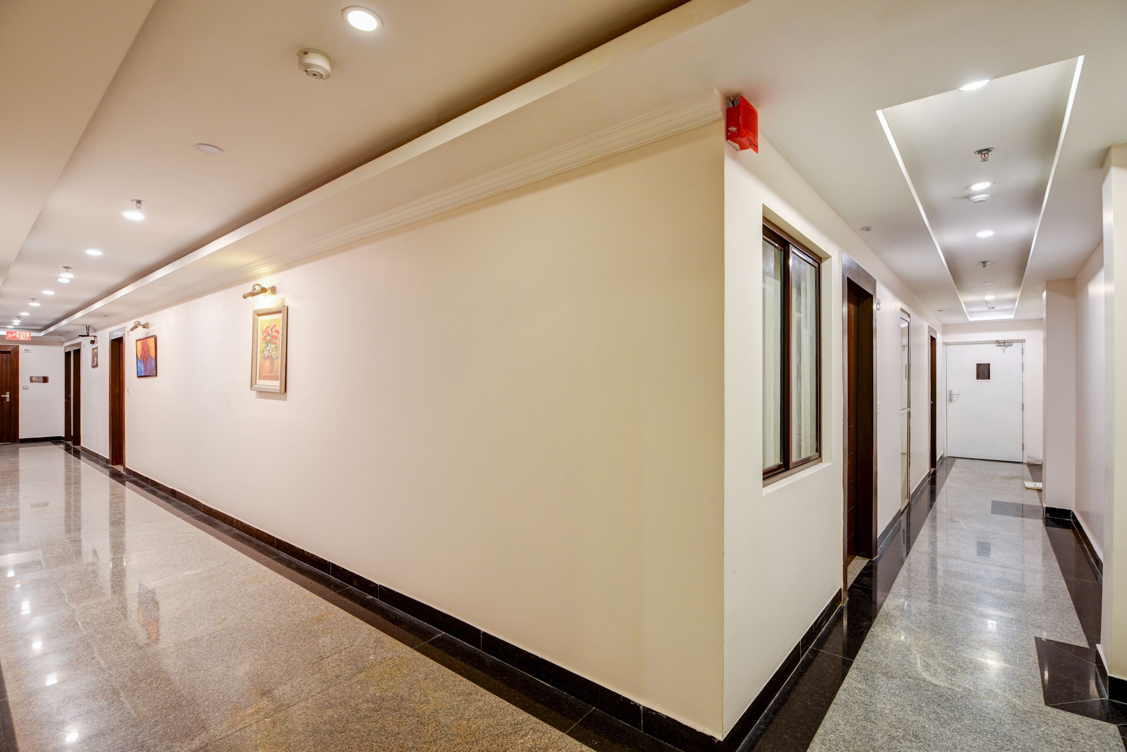 A long, well-lit hallway with a polished floor, framed artwork on the walls, and a door at the end.