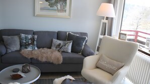 A living room with a grey sofa, a white armchair, a small round table, and a lamp.