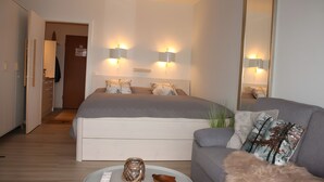 A bedroom with a bed, bedside lamps, a sofa, a mirror, and a small table with decorative items.