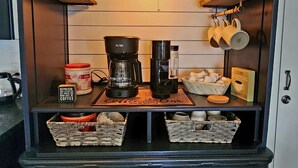 Uma cozinha com estação de café, incluindo cafeteira, xícaras e uma placa com a inscrição 'Adoro xícaras grandes'.