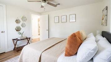 A bedroom with a bed, a ceiling fan, a door, and a wall with framed pictures.