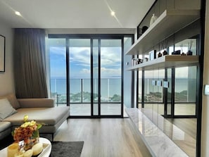 Ein modernes Wohnzimmer mit einer Couch, einem Couchtisch mit Blumen und einer großen Schiebeglastür, die auf einen Balkon mit Meerblick führt.