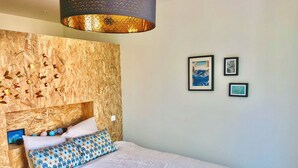 Een slaapkamer met een houten hoofdbord, een bed met gekleurde kussens en kunstwerken in lijsten aan de muur.