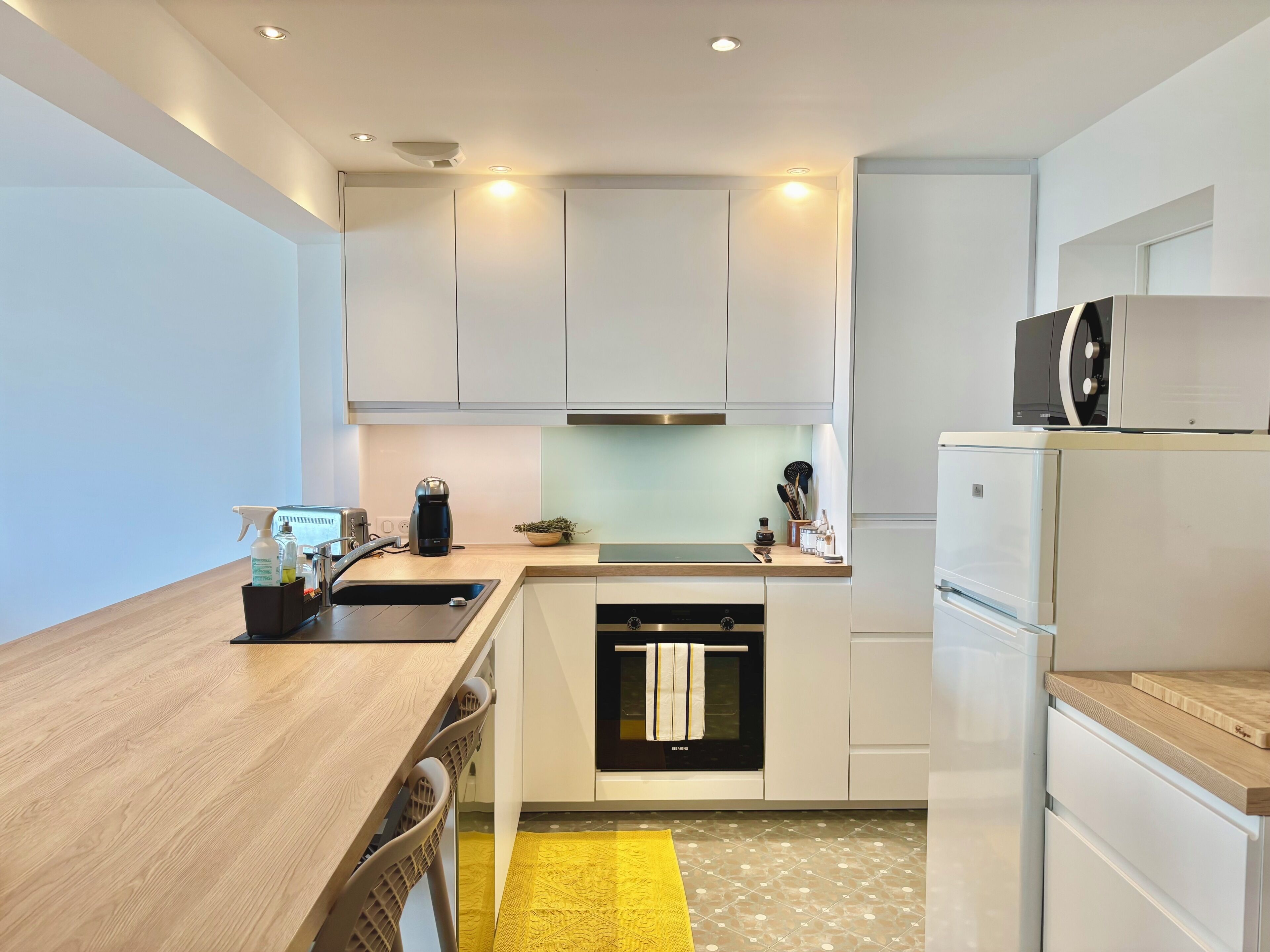 A modern kitchen with white cabinets, a built-in oven, a microwave, and a sink.