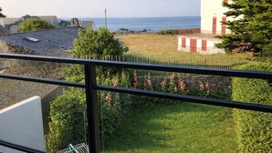 Een balkon met uitzicht op zee, een stenen muur met bloemen, en een gebouw met rode luiken.