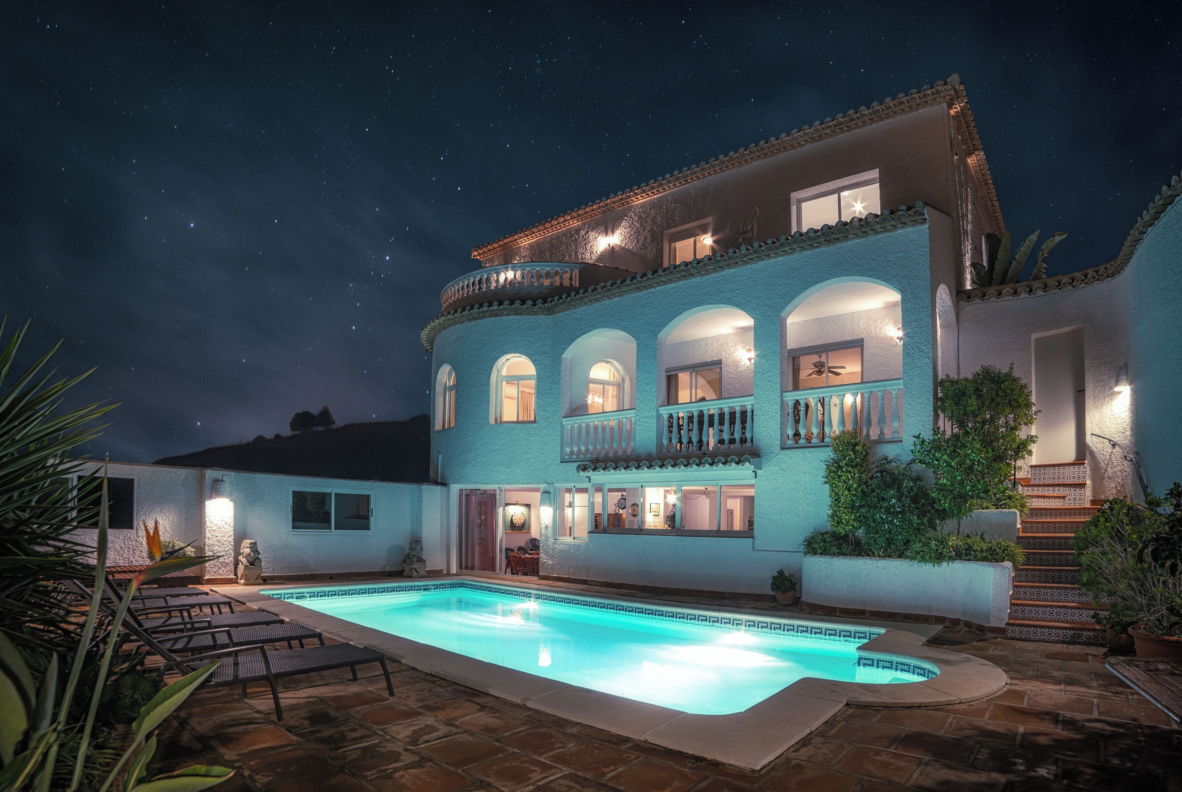 A two-story building with a swimming pool, multiple balconies, and a starry night sky.